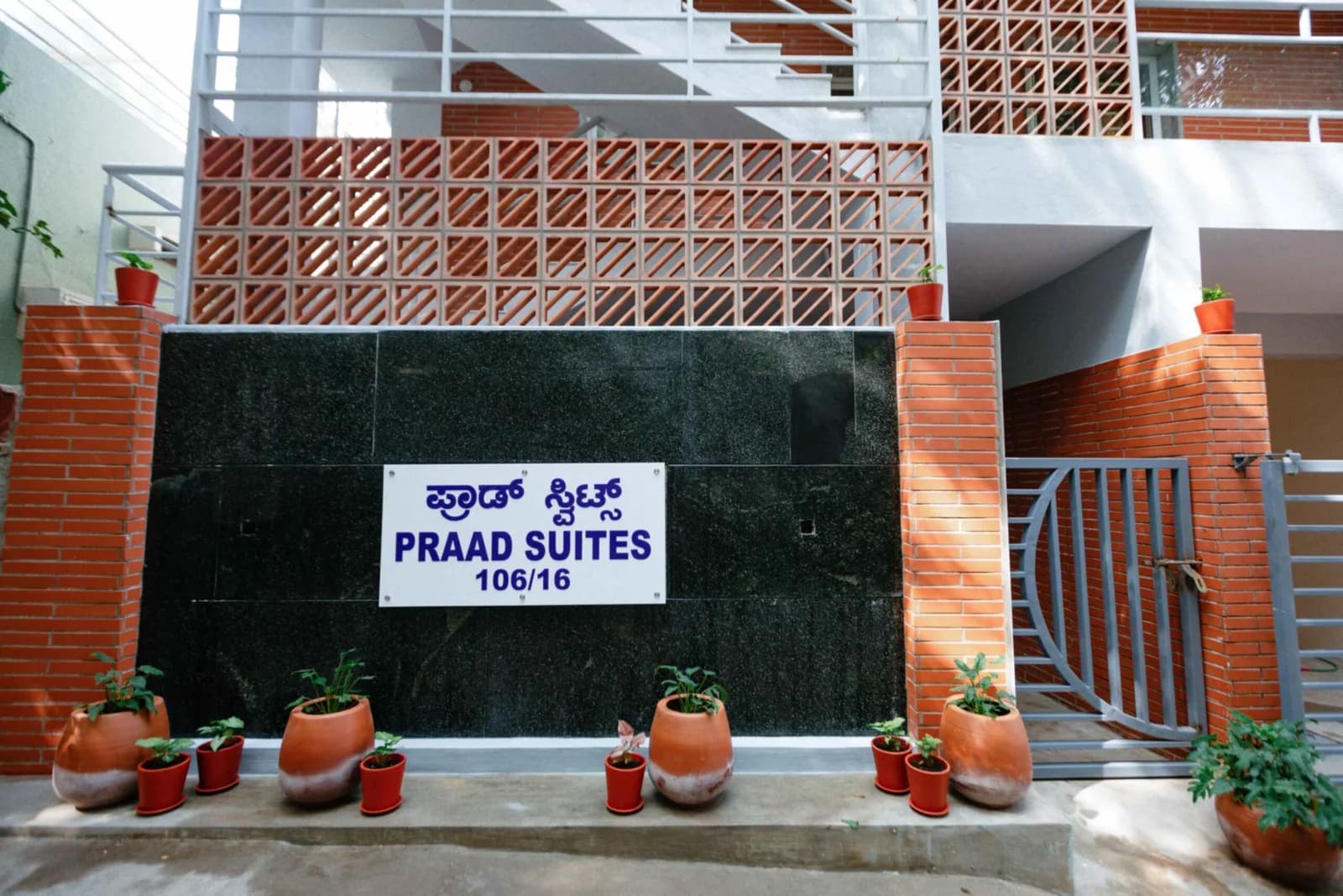 PRAAD Suites — the name board in granite between brick piers, under the jaali screen and the open stair